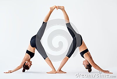 Two young women doing partner yoga asana downward facing dog Stock Photo