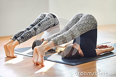 Two young women doing yoga asana plow pose Stock Photo