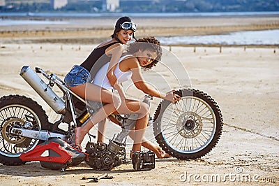 Two young women have fun playing on a disassembled motorcycle Stock Photo