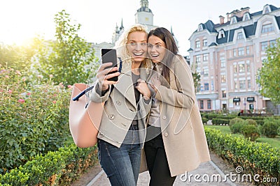 Two young women having fun, looking at the smartphone laughing, sunny autumn day, city background, golden hour Stock Photo