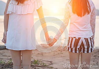 Two young women hold hands together on seaside Stock Photo