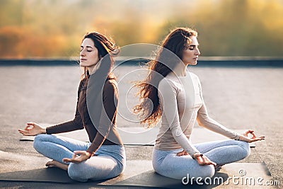 Two young women meditating in Lotus Pose on the roof outdoor Stock Photo