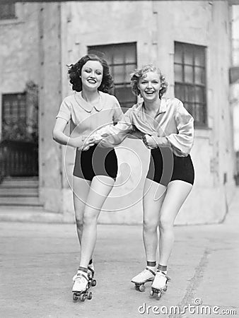 Two young women with roller blades skating on the road and smiling Stock Photo