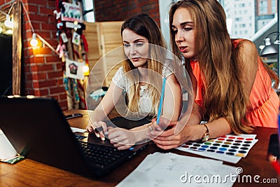 Two young women working on new creative design using laptop discussing ideas at cozy stylish studio Stock Photo
