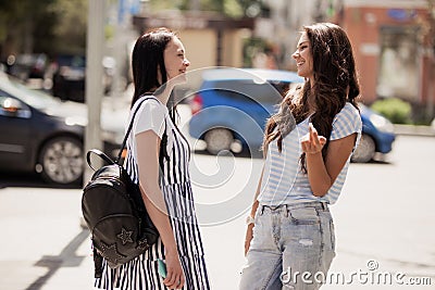 Two youthful pretty slim girls,wearing casual outfit,stand at the street and chat. Stock Photo