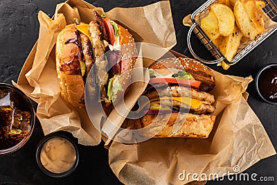 Two yummy grilled chicken burgers in a craft box, fries and cola on a dark background, top view. Hamburger and French fries. Stock Photo