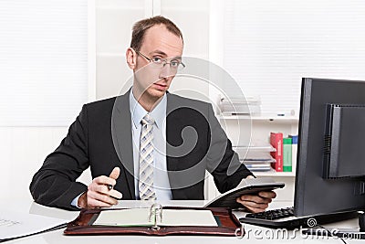 Typical examiner or controller - arrogant and disagreeable sitting at desk with computer Stock Photo