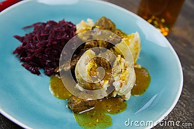 Typical german hearty meal: closeup of dumplings with brown sauce, red cabbage, goulash meat on blue china dish Stock Photo