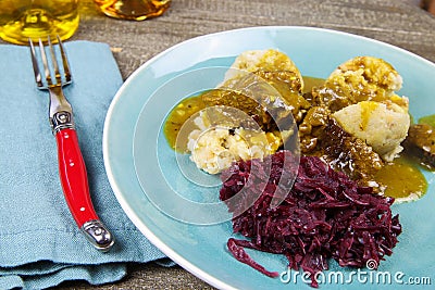 Typical german hearty meal: closeup of dumplings with brown sauce, red cabbage, goulash meat on blue china dish Stock Photo