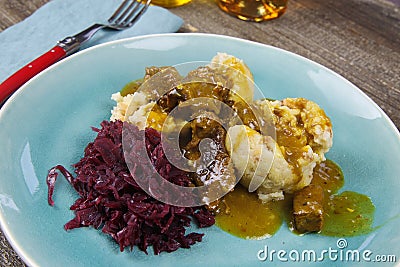 Typical german hearty meal: closeup of dumplings with brown sauce, red cabbage, goulash meat on blue china dish Stock Photo