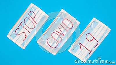 Typical 3-ply white surgical mask with rubber earhooks to cover mouth and nose with English block letters Stop Covid-19 on a blue Stock Photo