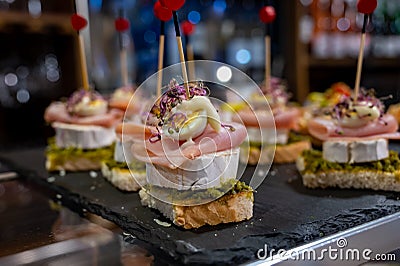 Typical snack of Basque Country, pinchos or pinxtos skewers with small pieces of bread, sea food, eggs, cheese, jamon served in Stock Photo