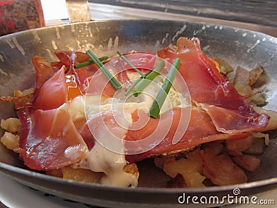 Typical South Tyrolean dish served pan fried with speck, mountain cheese, eggs, potatoes and chive Stock Photo