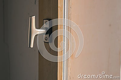 Typical window knob mounted on a wooden window frame in closed position. Metal contemporary modern knob or hook for opening the Stock Photo