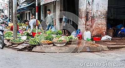 Typically Asian street corner vegetable market with selection of fruits and vegetables in path in front grimy building Editorial Stock Photo