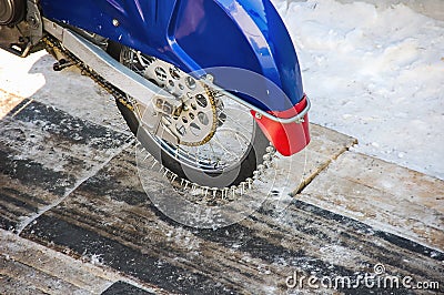 Tyre of motocross bike on ice and snow on background. Special winter tire with studs for riding on ice Stock Photo