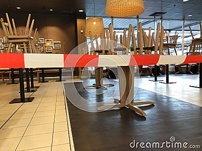 View beyond red white donÂ´t cross line in empty closed restaurant with chairs stapled on tables during corona crisis Editorial Stock Photo