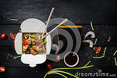 Udon stir fry noodles with seafood in a box on black background. With chopsticks and box for noodles. Stock Photo