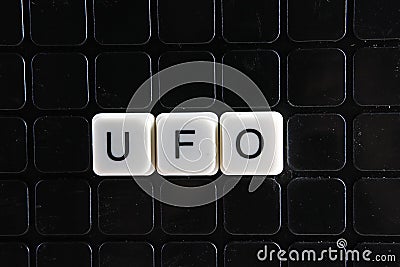 UFO control text word title caption label cover backdrop background. Alphabet letter toy blocks on black reflective background. Stock Photo