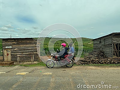 Typical roadside scene, with two men on a motorbike driving through a rural village Editorial Stock Photo