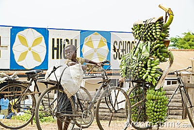 Boy with heavy load on his bike in Uganda. Boy carrying loads on bike. Bicycles loaded with plantains, cooking bananas and bags Editorial Stock Photo