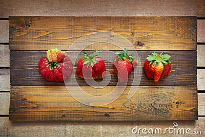 Ugly food. Strange deformed strawberries on wooden background. Misshapen produce, food waste problem concept. Stock Photo