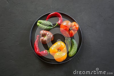 Ugly organic colorful tomato, pepper, cucumber in plate on black concrete. Concept organic vegetables Stock Photo