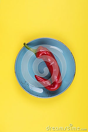 Ugly red chili peppers on a blue plate on a yellow background, minimal style of nature, pop art, creative food concept, modern art Stock Photo