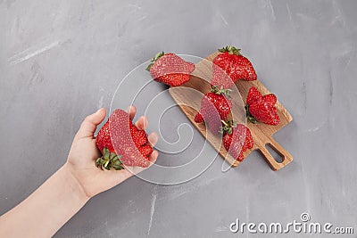 Ugly strawberries on a wooden serving board. A fresh, ripe funny-shaped strawberry lies in a child`s hand Stock Photo