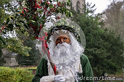 Father Christmas robed in green, masked and carrying holly branc Editorial Stock Photo