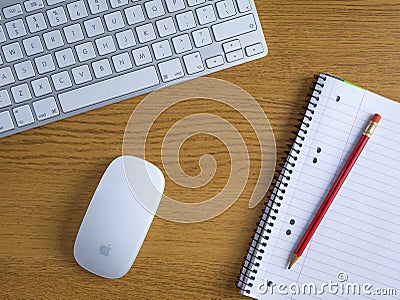 UK, October 2019: Apple mac wireless mouse and keyboard on wooden desk with notepad and pencil Editorial Stock Photo