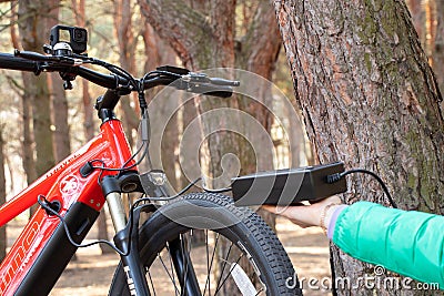 Ukraine Dnipro 05.04.2021 - a red electric bike is recharged in a forest in a park, new technologies Editorial Stock Photo