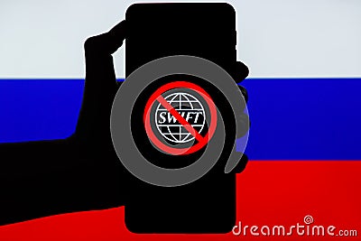 Ukraine, Kiev - February, 23 2022: Silhouette of black hand holding mobile with crossed out SWIFT logo and Russian flag Editorial Stock Photo