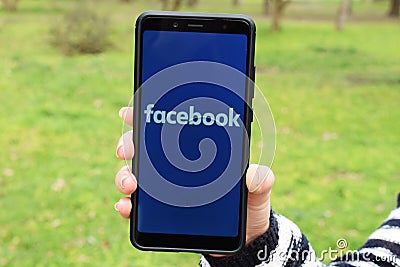 Ukraine, Kremenchug - April, 2019: Girl with smartphone in her hand and a Facebook logo on the screen. Social network Editorial Stock Photo