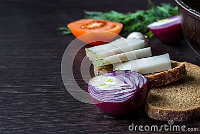 Ukrainian national food is lard salo with bread with red onions on the background of the tomato with garlic on wooden table. Stock Photo