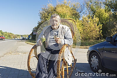 ukrainian senior man sitting in rrocking chair on roadside and holding vacuum bottle Stock Photo