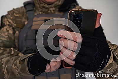 Ukrainian soldier in military pixel unform and bulletproof vest jacket with banner of flag of Ukraine holding smartphone Stock Photo