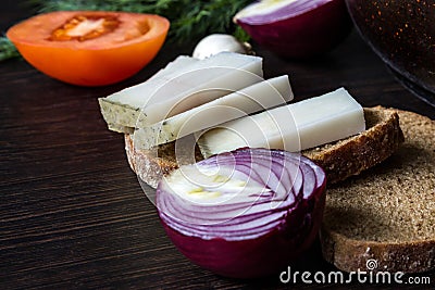 Ukrainian traditional food is lard salo with bread with red onions on the background of the tomato with garlic on wooden table Stock Photo