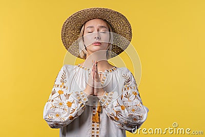 Ukrainian woman praying for Ukraine, victory, peace on yellow background. Girl begs God to save country, people Stock Photo