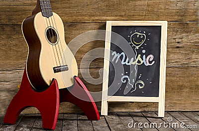 Ukulele guitar and blackboard with the word Music written on wooden background Stock Photo