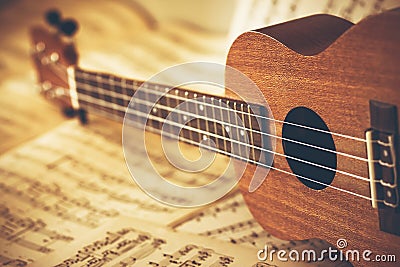 An ukulele lies on scattered sheets of paper with notes on it. Music lessons and learning solfeggio Stock Photo