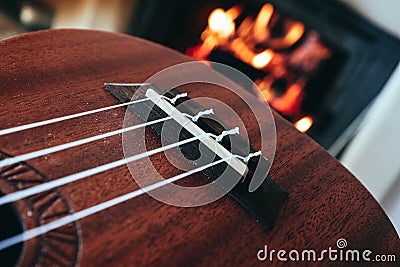 Ukulele small guitar close up stings, fireplace on the background. Musical concept, guitar fret board macro, fire in chimney, cos Stock Photo