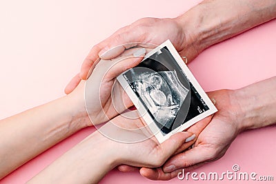 Ultrasound image pregnant baby photo. Woman hands holding ultrasound pregnancy picture on pink background. Pregnancy Stock Photo