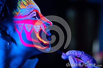 Ultraviolet black light glowing bodyart processing on young woman`s face. Pink and purple dyes in cold blue light Stock Photo