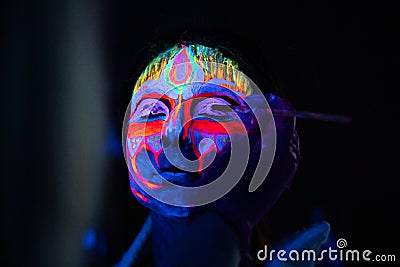 Ultraviolet black light glowing bodyart processing on young woman`s face. Pink and purple dyes in cold blue light Stock Photo