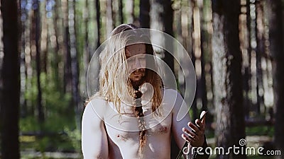 Um guerreiro com cabelo longo e um torso desencapado olha na reflexão em uma grande lâmina Viking olha sua arma filme Um guerreiro com cabelo longo e um torso desencapado olha na reflexão em uma grande lâmina Viking olha sua arma filme