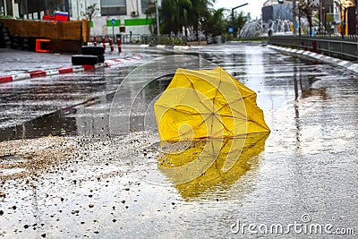 An umbrella broken by the wind with raindrops on the wet asphalt road. Winter weather in Israel: rain, puddles with water circles Stock Photo