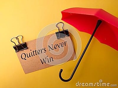 Umbrella and brown card with text Quitters Never Win Stock Photo