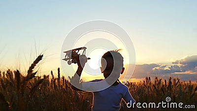 Un enfant heureux court à travers un champ de blé pendant le coucher du soleil, tenant un avion de jouet Le garçon montre le vol banque de vidéos Un enfant heureux court à travers un champ de blé pendant le coucher du soleil, tenant un avion de jouet Le garçon montre le vol banque de vidéos