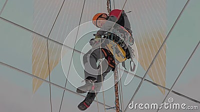 Un escalador industrial en una escalera está preparando una cuerda para levantar el equipo Un trabajador con un casco protector h metrajes Un escalador industrial en una escalera está preparando una cuerda para levantar el equipo Un trabajador con un casco protector h metrajes